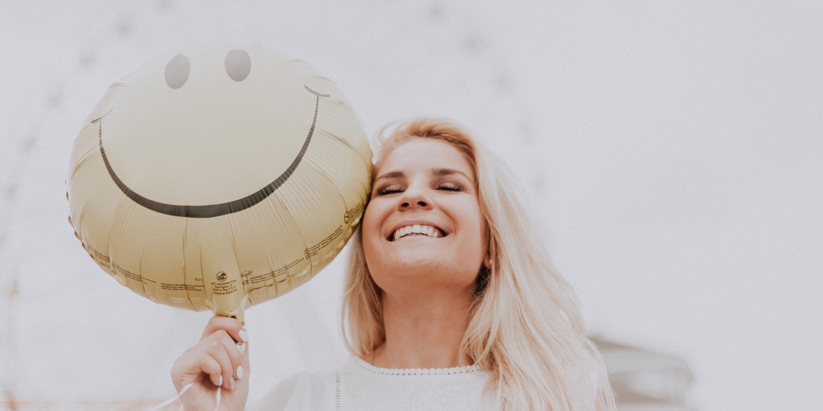 Frau lacht mit Smiley-Luftballon in der Hand